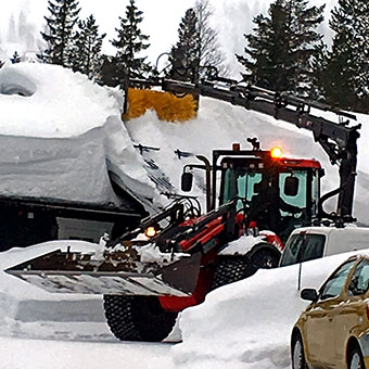 Sopvals gräv monterad på traktor. Sopvalsen borstar av snö från tak. 